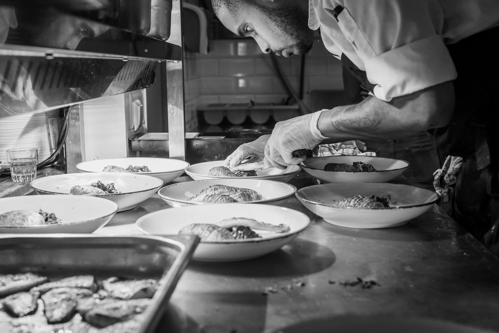 Manos emplatando en el pase de la cocina, en blanco y negro