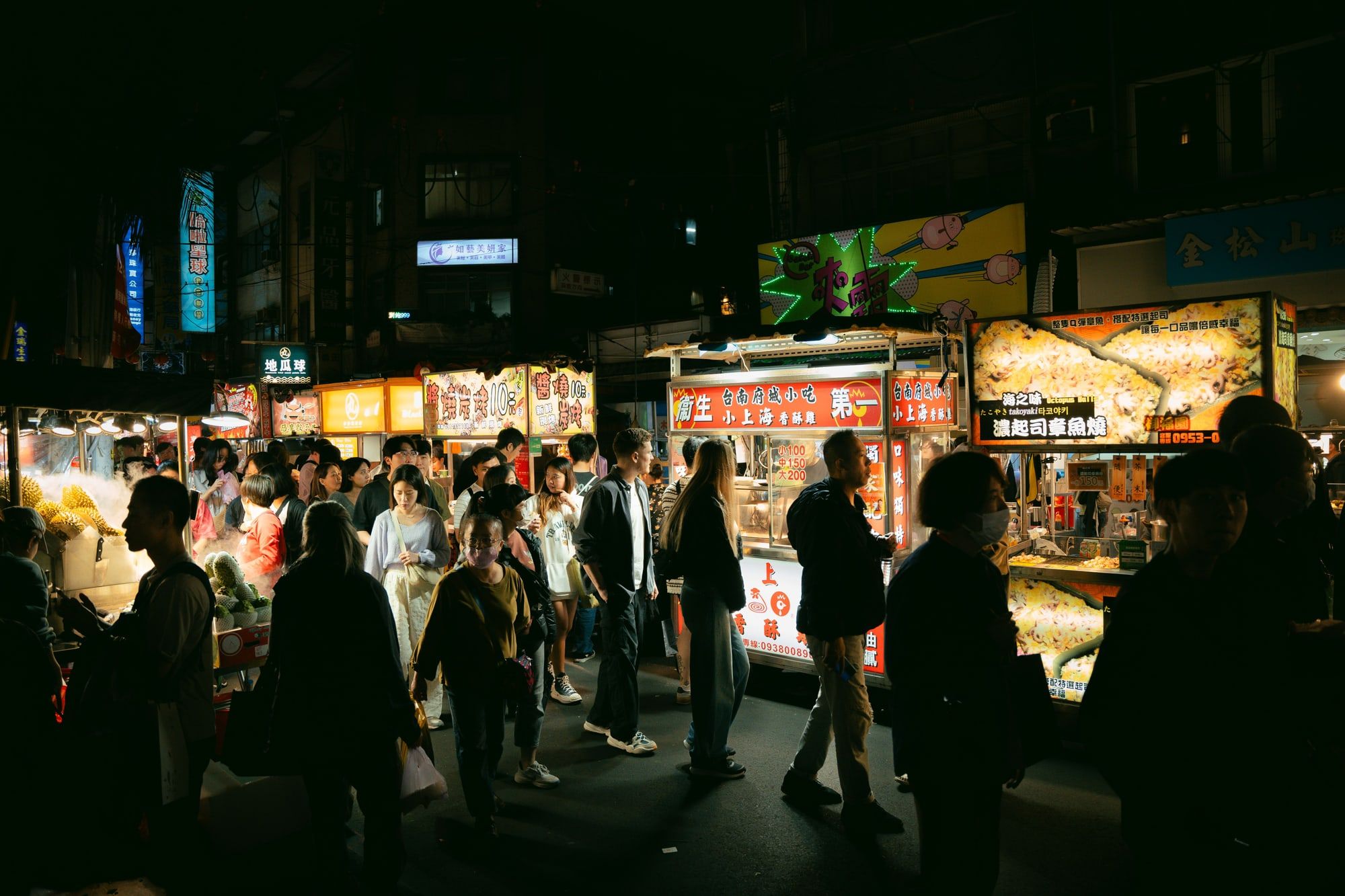 Un mercado nocturno lleno de gente, con los puestos de comida encendidos y carteles de colores