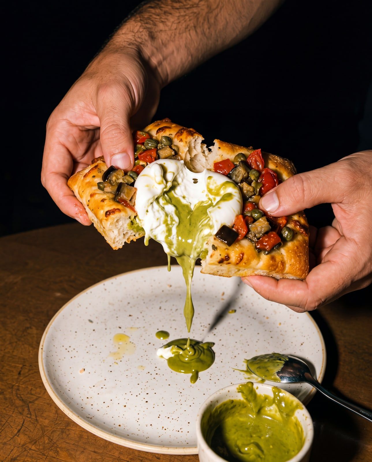 Manos abriendo una focaccia con burrata recién horneada