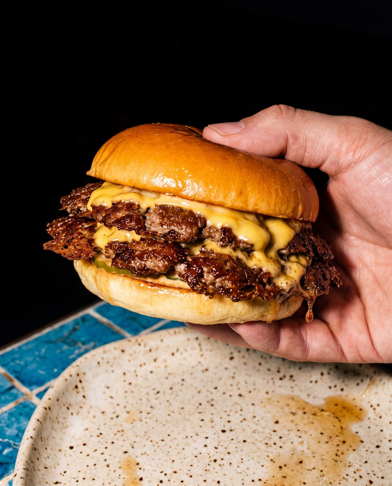 Smashburger doble con cheddar fundido, en las manos